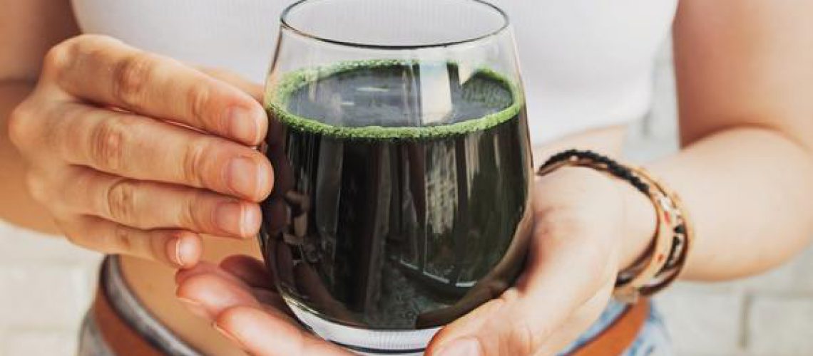 Woman holding Glass of Green Juice - Spirulina Health Benefits